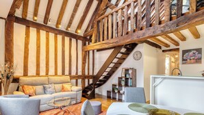 Un intérieur rustique avec des poutres apparentes, un escalier, un canapé, une table à manger avec des sets de table et une bibliothèque.