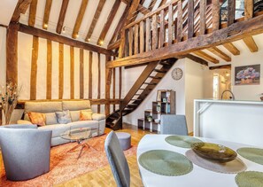 Ein rustikales Interieur mit freiliegenden Holzbalken, einer Treppe, einer Couch, einem Esstisch mit Platzsets und einem Bücherregal.