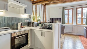 Une cuisine moderne avec des armoires blanches, un four encastré, un four à micro-ondes et un grille-pain. Une fenêtre avec des rideaux offre une vue sur les bâtiments environnants.