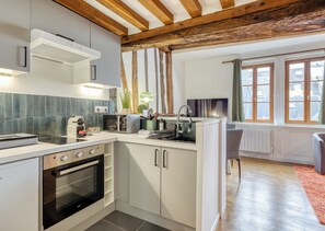 Eine moderne Küche mit weißen Schränken, einem eingebauten Backofen, einer Mikrowelle und einem Toaster. Ein Fenster mit Vorhängen bietet Blick auf Gebäude.