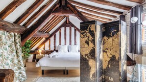 Une chambre avec un plafond en bois, un lit, un mur décoré d’une carte et un globe terrestre.