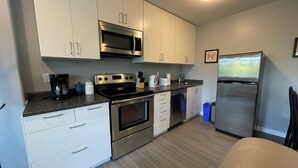 Una cocina moderna con electrodomésticos de acero inoxidable, armarios blancos y piso de madera.