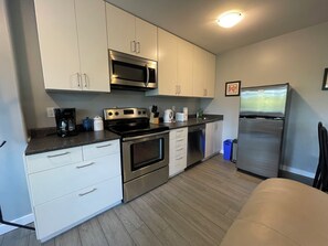 Una cocina moderna con electrodomésticos de acero inoxidable, armarios blancos y piso de madera.