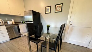 Una cocina moderna con una mesa de comedor de vidrio, sillas negras, un lavavajillas de acero inoxidable y un refrigerador.