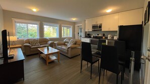 Un espacio habitable compacto con kitchenette, un conjunto de sofás, una mesa de comedor y un televisor.