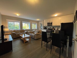 Un espacio habitable compacto con kitchenette, un conjunto de sofás, una mesa de comedor y un televisor.