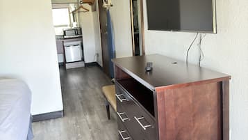 Habitación de hotel compacta con cama, escritorio con cajones, televisor y una kitchenette al fondo.