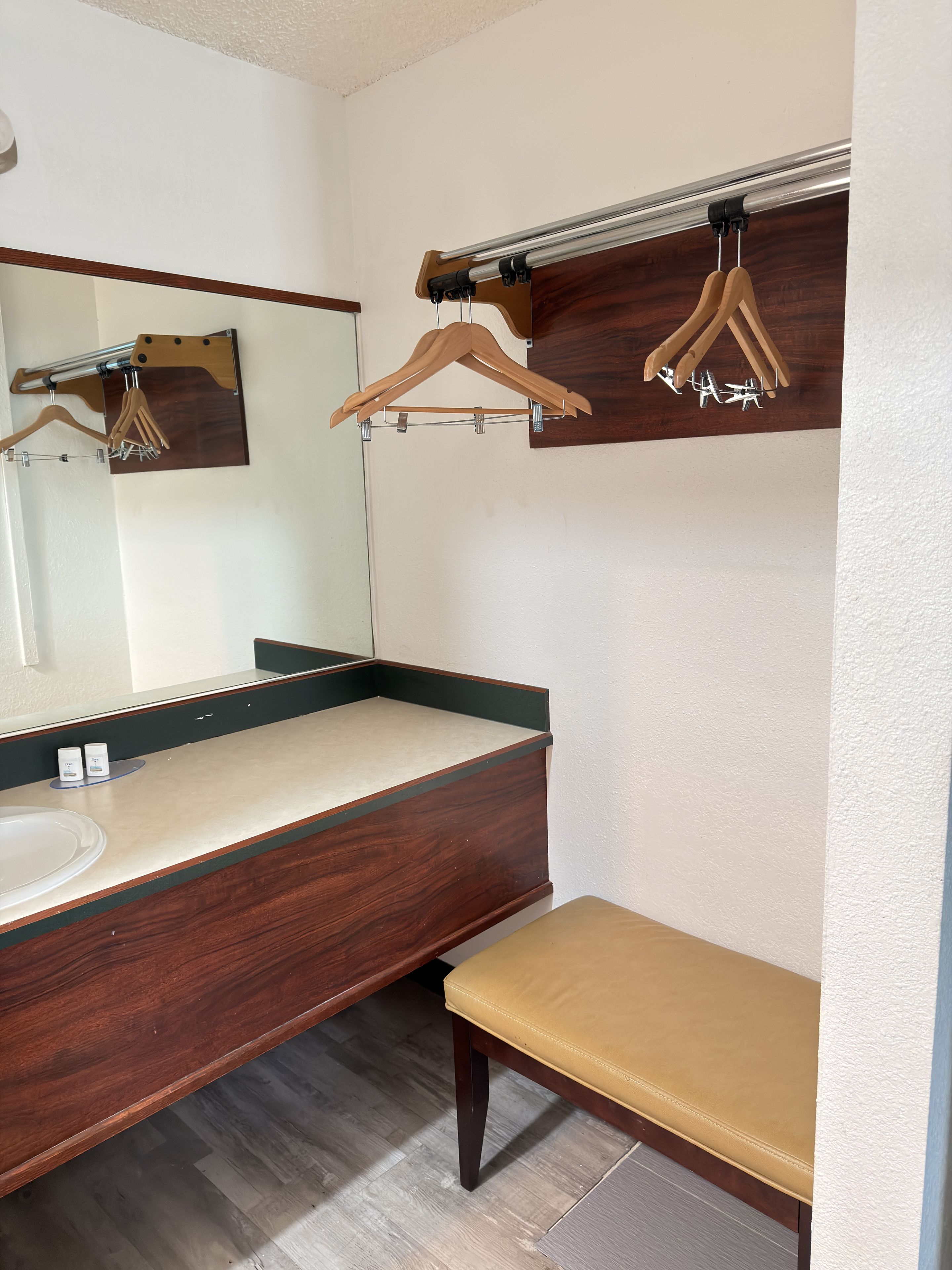 A bathroom with a wooden vanity, a bench, a mirror, and wooden hangers.