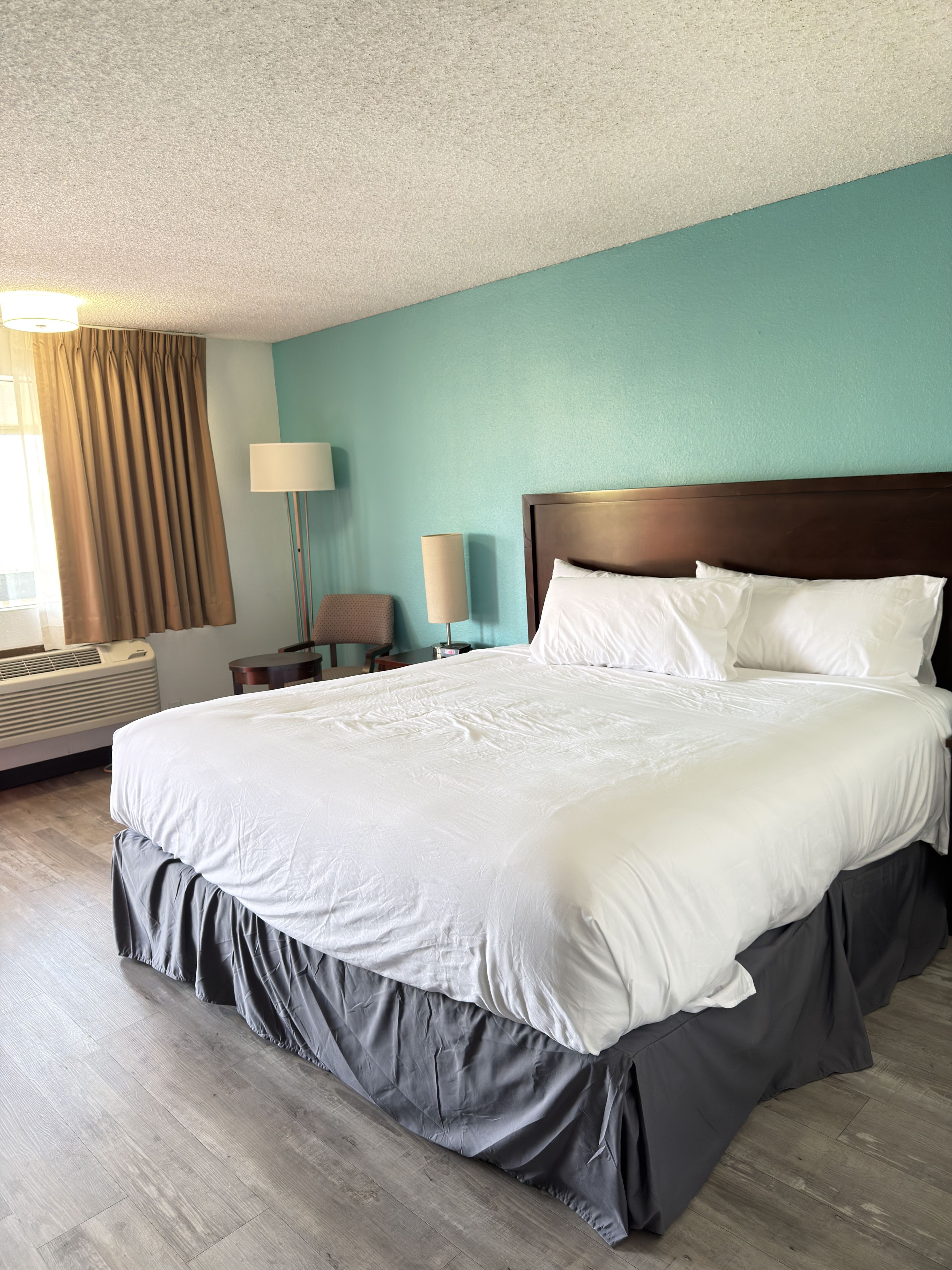 A hotel room with a large bed, a bedside table, a lamp, and a window with curtains.