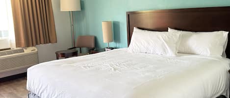 A hotel room with a large bed, a bedside table, a lamp, and a window with curtains.