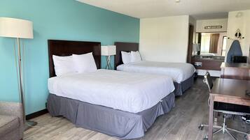 A hotel room with two beds, a desk, a chair, and a lamp.