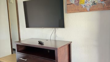 Een kamer met een aan de muur bevestigde televisie, een houten kast met lades, een bankje en een decoratief kunstwerk met nummerborden van een staat.