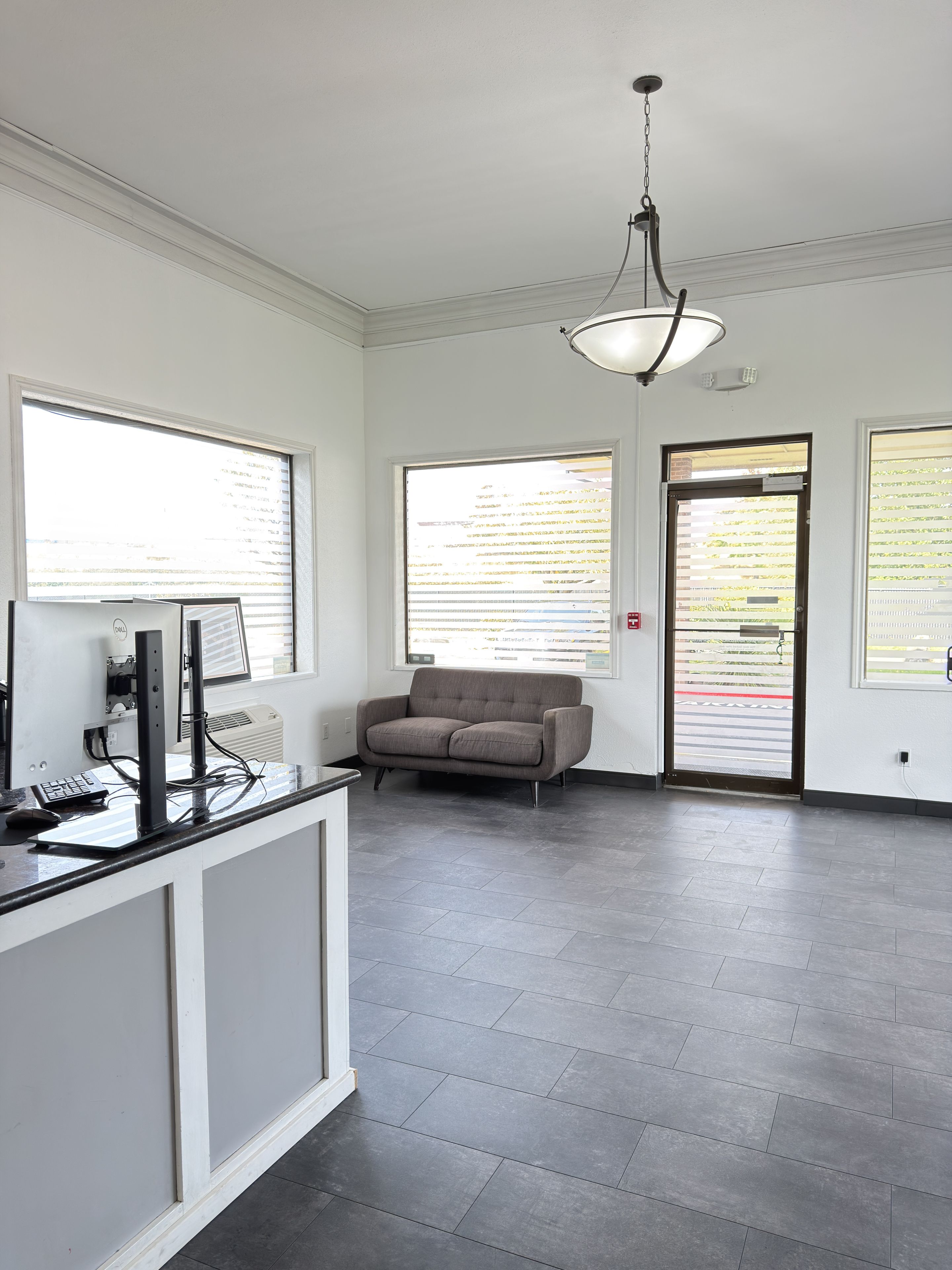 A modern office space with a desk, computer, and chair. There are large windows and a door with a view of the outside.