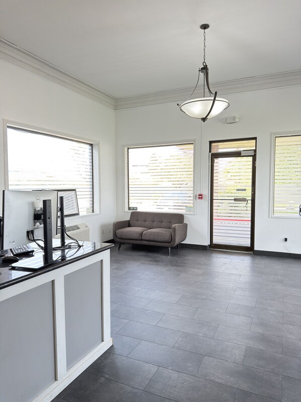 A modern office space with a desk, computer, and chair. There are large windows and a door with a view of the outside.