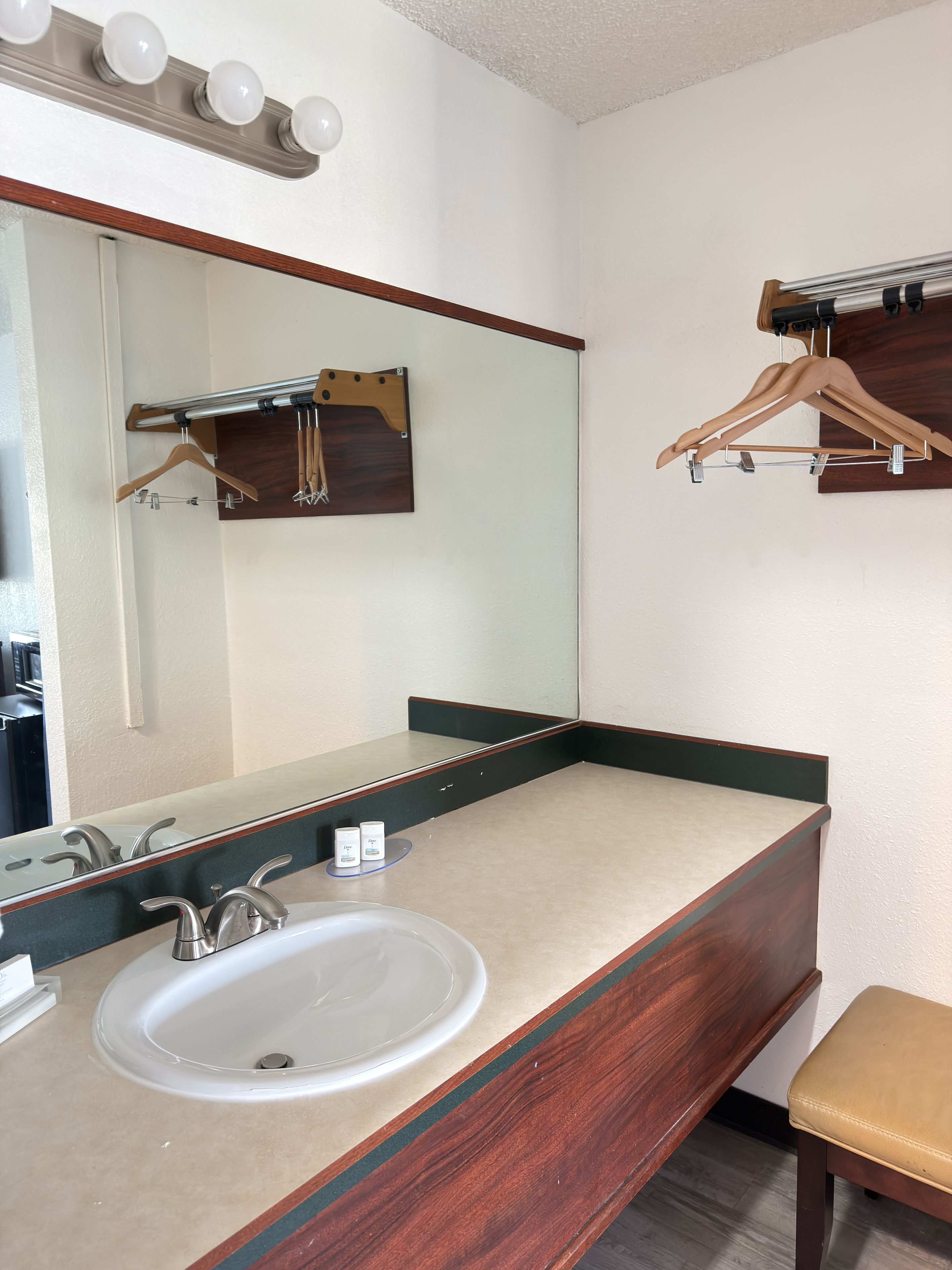 Een badkamer met een wastafel, spiegel, houten handdoekrek en een houten kruk.