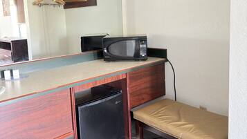 Une petite cuisine équipée comprenant un four à micro-ondes, un petit réfrigérateur, un banc et une étagère en bois avec des porte-manteaux.