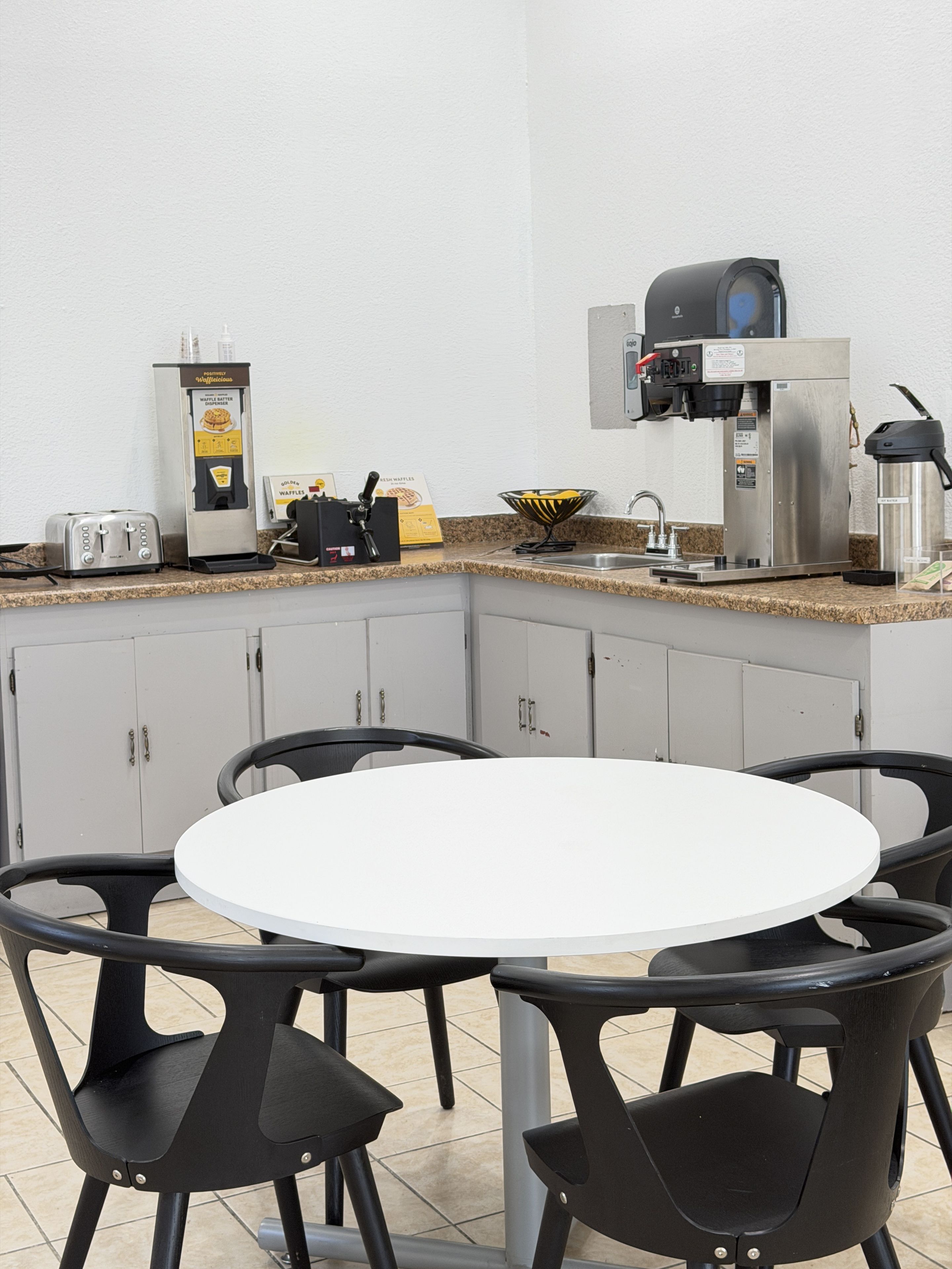 A corner kitchen area with a waffle maker, coffee machine, toaster, and a bowl of waffles on the counter.