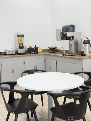 A corner kitchen area with a waffle maker, coffee machine, toaster, and a bowl of waffles on the counter.