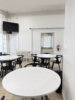 A room with white walls, a flat-screen TV mounted on the wall, a window with blinds, and a fire extinguisher on the wall. - Legacy Inn Kent (Kent)