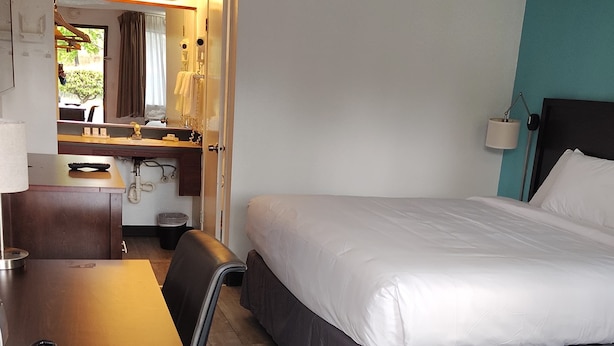 A hotel room with a bed, a desk with a chair, a bathroom with a mirror, and a door leading to another room.