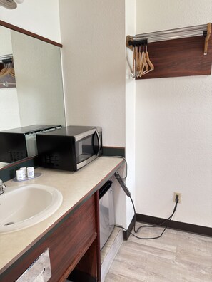 A bathroom with a sink, mirror, microwave, and a towel rack.
