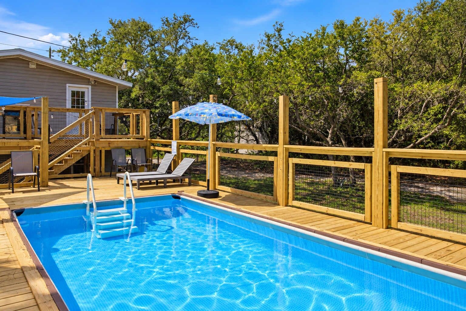 A wooden deck with a swimming pool, lounge chairs, and a covered area with an umbrella.