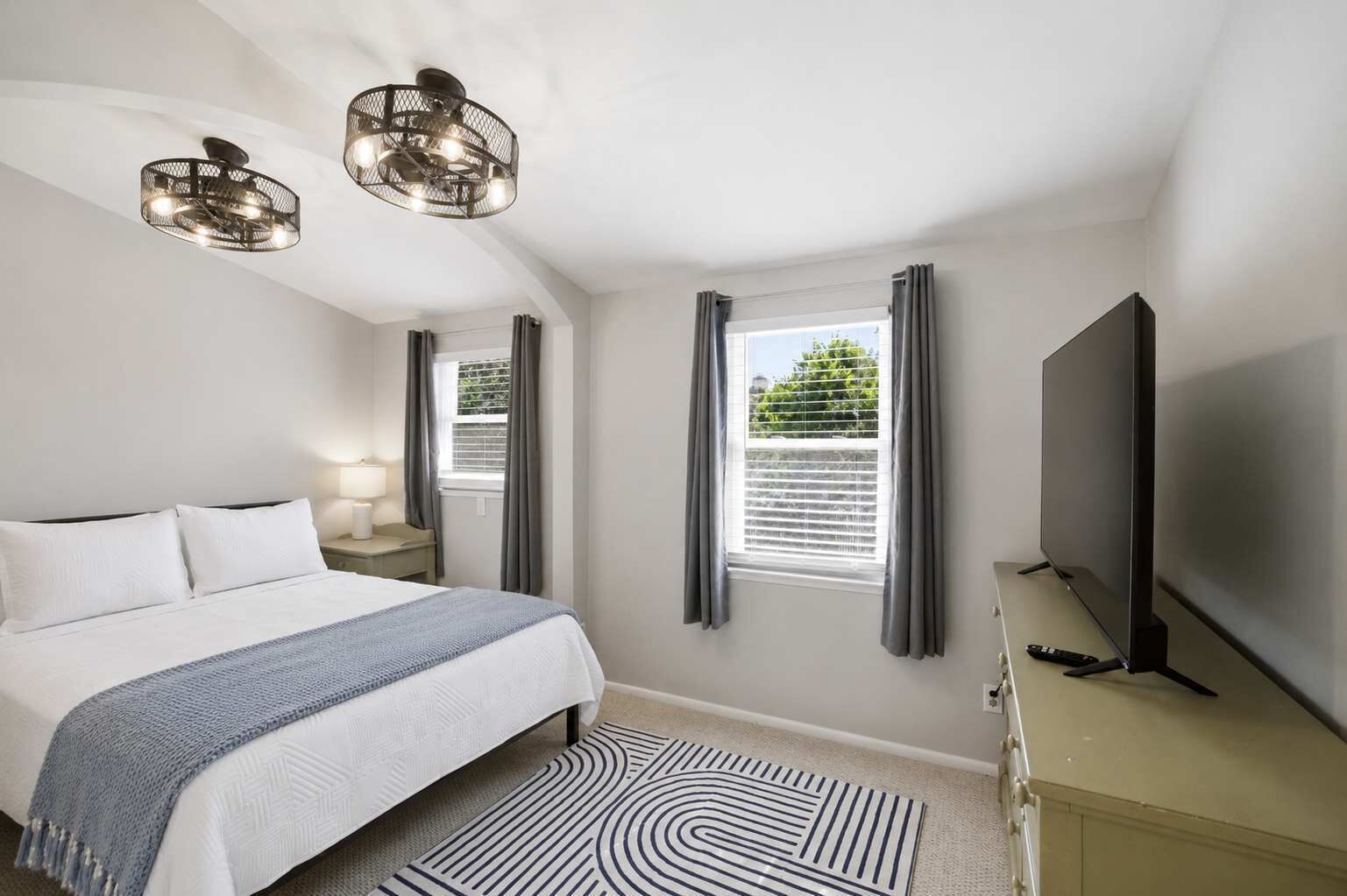 A bedroom with a bed, a TV, a lamp, and a window with curtains.