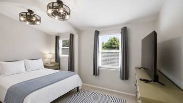 A bedroom with a bed, a TV, a lamp, and a window with curtains.