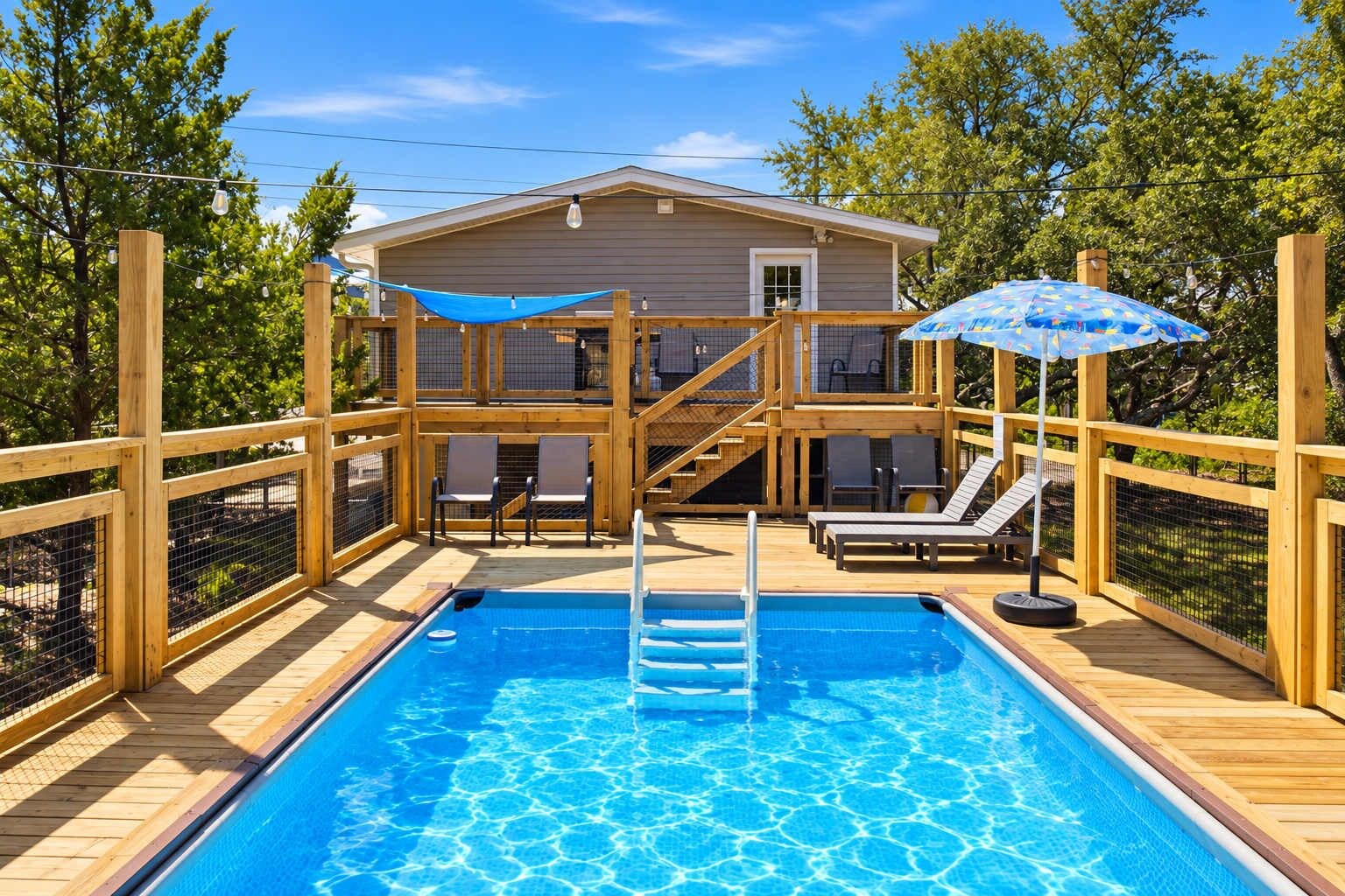 Una piscina con muelle de madera, sillas de descanso y una casa al fondo.