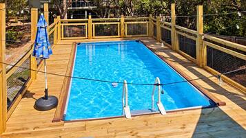 A rectangular swimming pool with a wooden deck, surrounded by a wooden fence and a rope barrier.