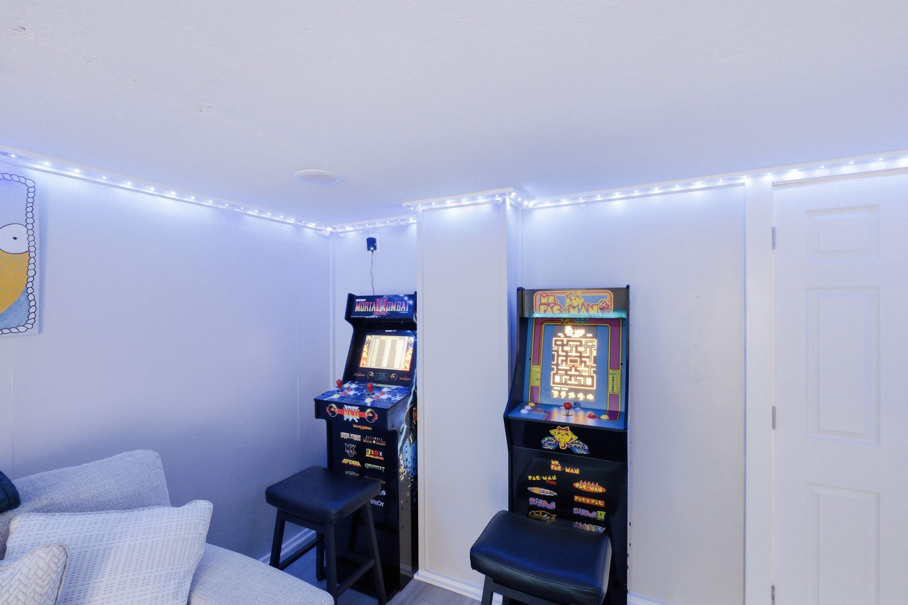 Una habitación con dos máquinas de videojuegos, una cama y una puerta.