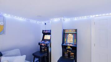Una habitación con dos máquinas de videojuegos, una cama y una puerta.