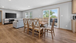 A modern living room with a sofa, wooden dining table, chairs, a TV, and a balcony with a view. - Private Countryside Escape • Deck Views • Near SA (Adkins)