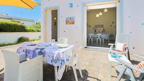Een buiten eethoek met een tafel voor twee personen, witte stoelen en een gele parasol.