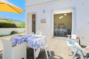 An outdoor dining area with a table set for two, white chairs, and a yellow umbrella. - Zaffiro by Casa di Marco (Torre Suda)