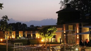 An outdoor dining area with tables and chairs, a building with a modern design, and a view of distant mountains. - Relais Du Silence Domaine La Charpiniere (Saint-Galmier)