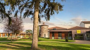 A building with a stone tower, wooden facade, and a sign indicating a restaurant. - Relais Du Silence Domaine La Charpiniere (Saint-Galmier)