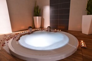 A hot tub with a tiled floor, surrounded by potted plants and candles. - Relais Du Silence Domaine La Charpiniere (Saint-Galmier)
