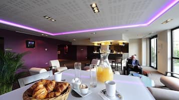 Un coin repas moderne, avec une table mise pour le petit-déjeuner, comprenant des croissants, du jus de fruits et du café.