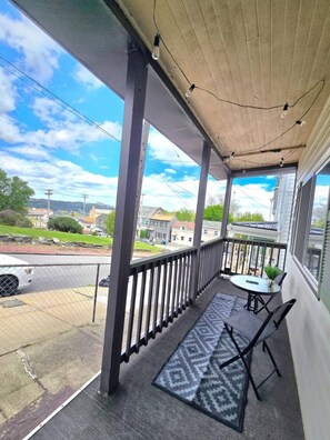 A covered balcony with a table and chairs, a doormat, and a view of the street and houses. - 3 bedroom home with a view, Minutes from Downtown Pittsburgh (Pittsburgh)