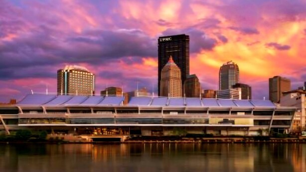 A modern building with a flat roof, a prominent tower with signage, and a reflection in the water. - 3 bedroom home with a view, Minutes from Downtown Pittsburgh (Pittsburgh)