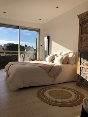 A bedroom with a large bed, a view through a sliding glass door, and a decorative wooden cabinet. - Magnificent 3-room apartment (Le Cannet)