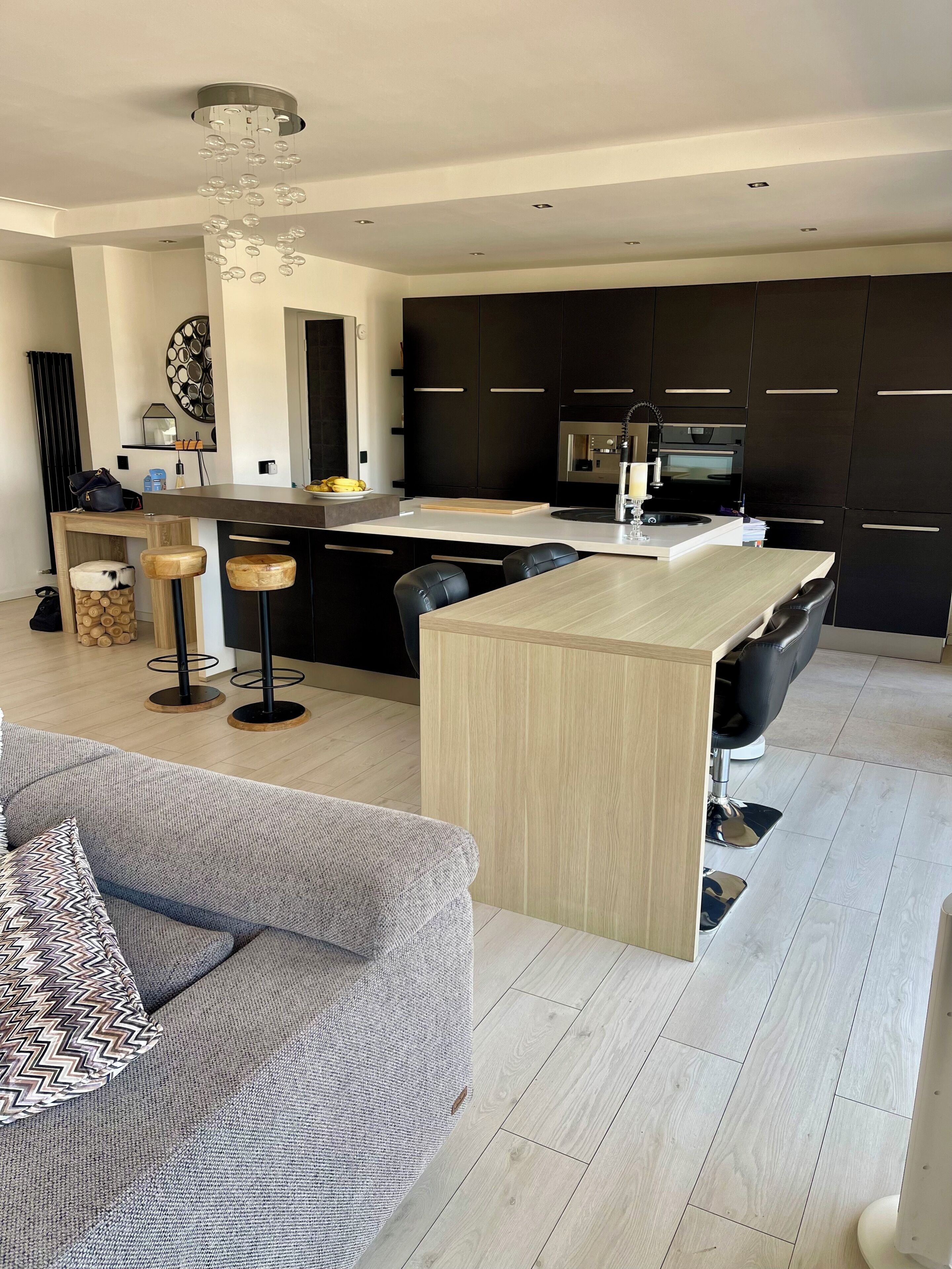Une cuisine moderne avec des meubles de couleur sombre, un îlot central et un coin bar.