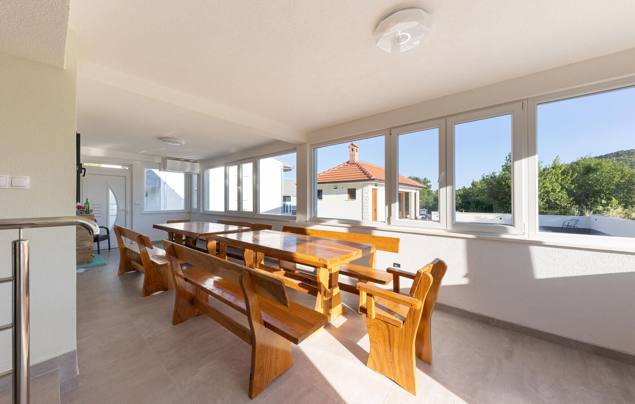 Un comedor amplio con ventanas grandes, vistas a un edificio con tejado rojo y una lámpara en el techo.