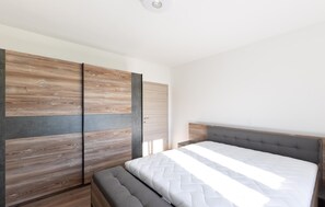 A bedroom with a bed, a grey upholstered bench, and a wardrobe with wooden panels. - Amazing home in Muc Gornji (Muc Gornji)