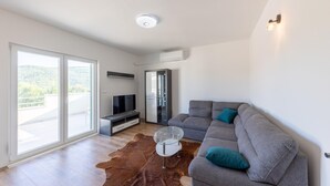 Un salon moderne avec un canapé gris, une table basse en verre, un téléviseur à écran plat et un meuble vitré.