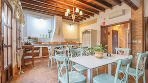 A dining area with tables and chairs, a kitchen in the background, and a staircase leading to another floor.