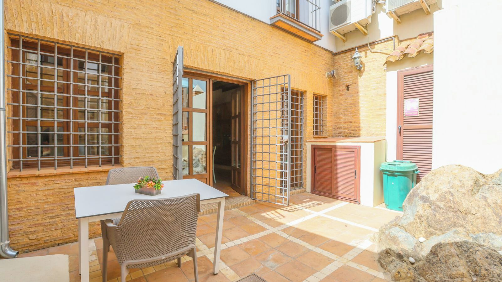Un patio con una mesa, sillas, una reja metálica y un basurero.
