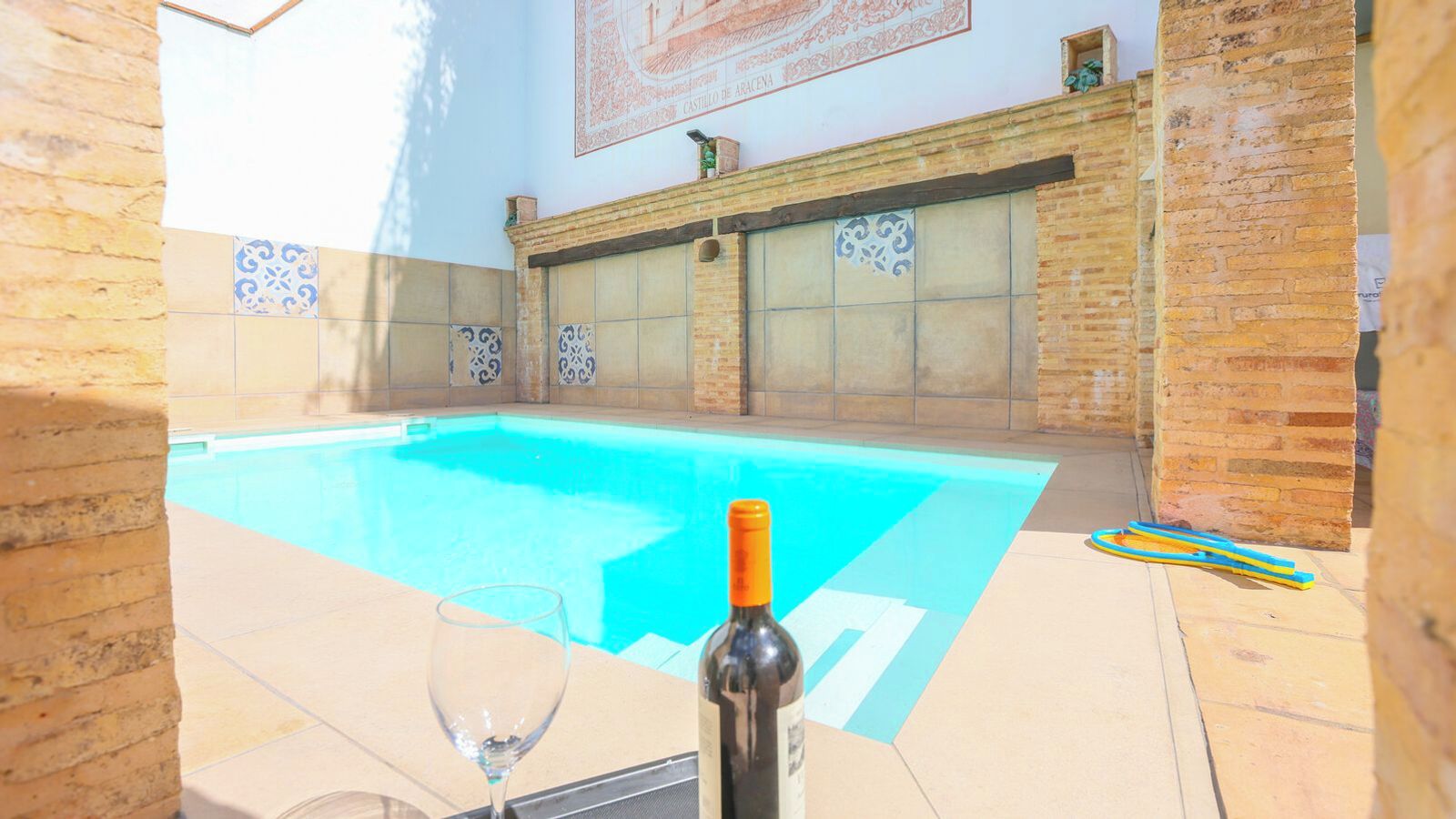 A swimming pool with a wine bottle and glass on the edge, surrounded by tiled walls and a brick structure.