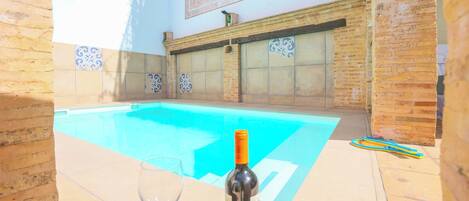 A swimming pool with a wine bottle and glass on the edge, surrounded by tiled walls and a brick structure.